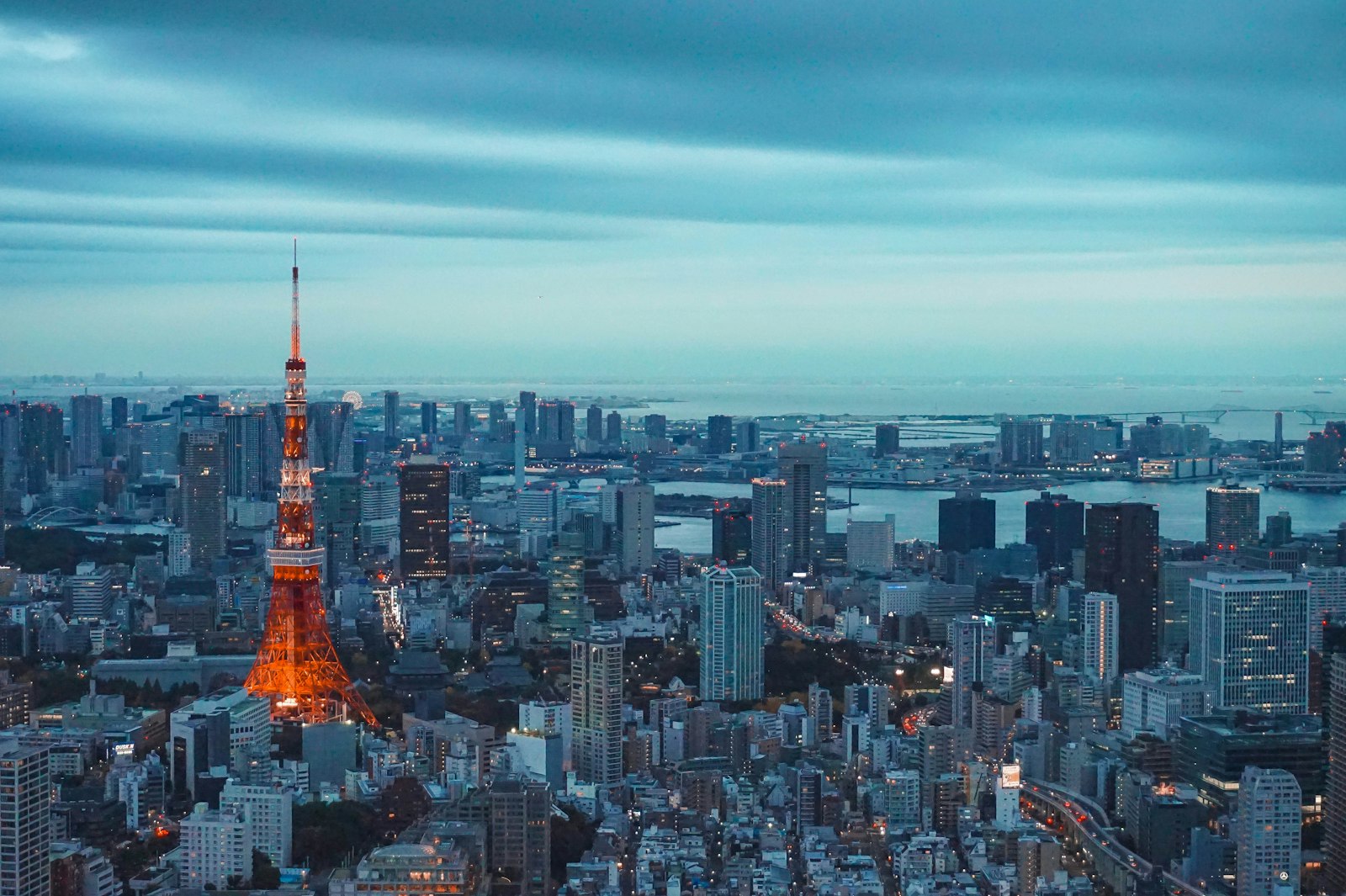 Tokyo Tower illuminated at dusk above a sweeping city skyline reaching to the bay